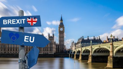 Bild på det kända engelska landmärket Big Ben. I förgrunden syns två skyltar som pekar åt olika håll, de symboliserar Brexit.
